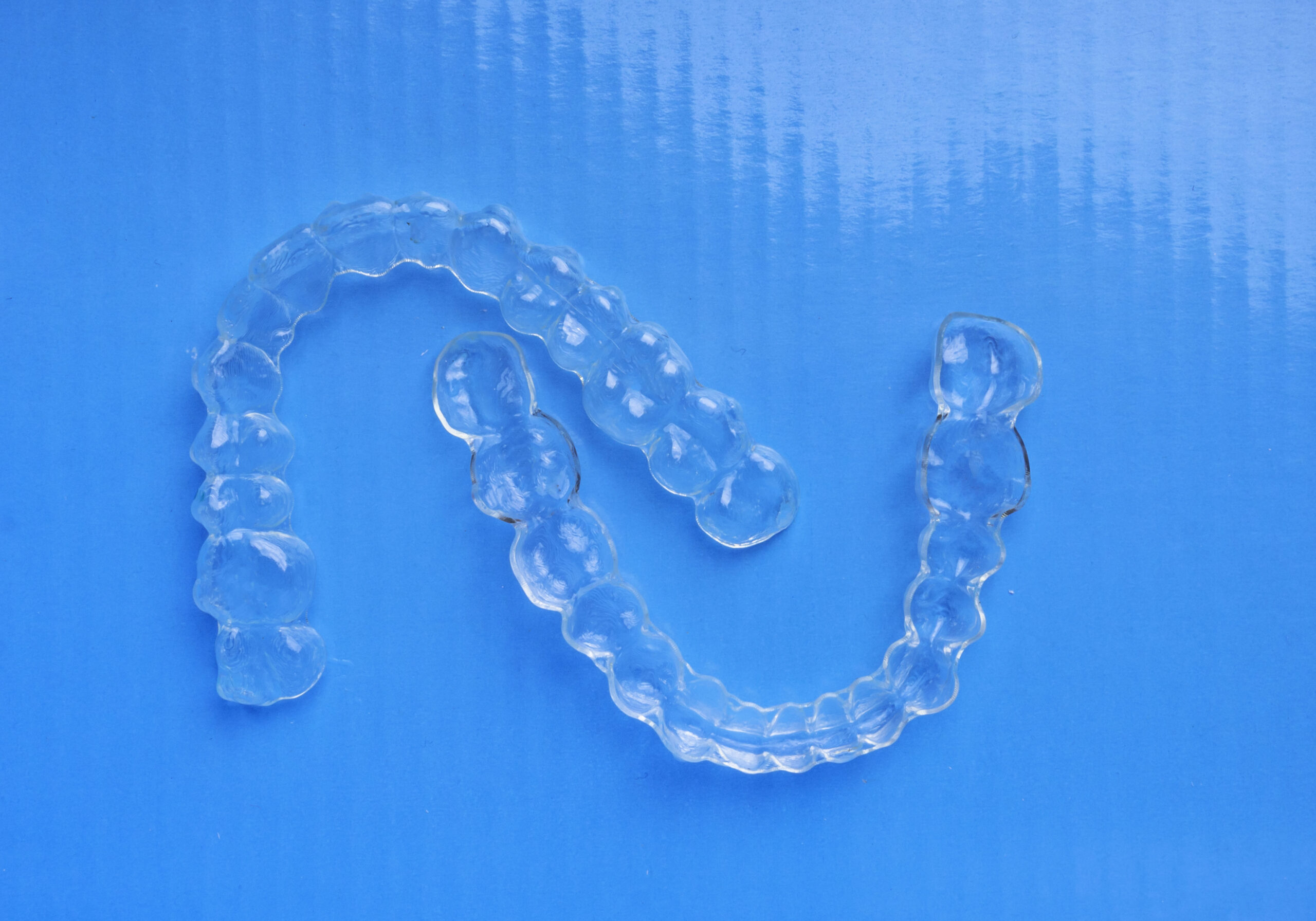 Invisible dental aligners, teeth brackets on blue background, Plastic braces dentistry retainers to straighten teeth. Transparent braces to straighten teeth in cosmetic dentistry and orthodontics. Used as individual tooth tray for whitening also.
